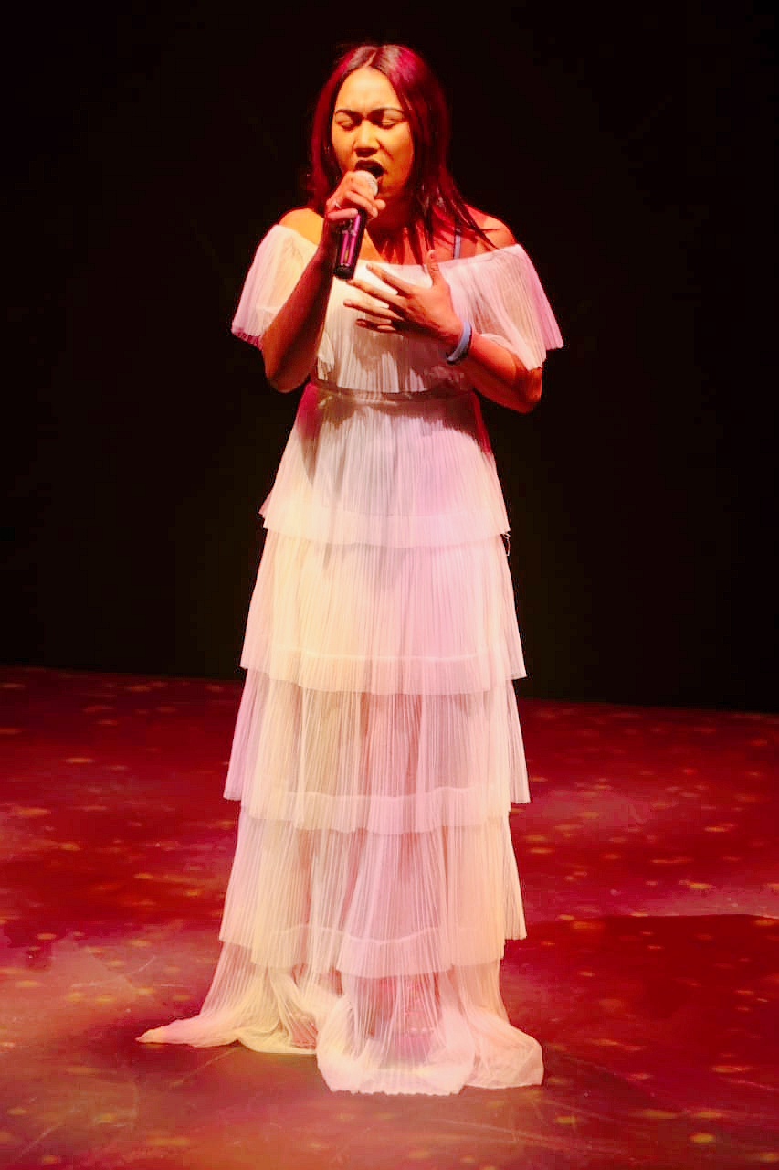 Estée singing on stage in a white gown